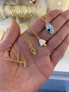Collares con dijes de luna, mano de Fátima (dorado y azul) y honguito (blanco). Al mayor